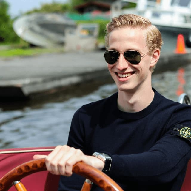 Ein junger Mann mit Sonnenbrille steuert ein Boot und lächelt dabei