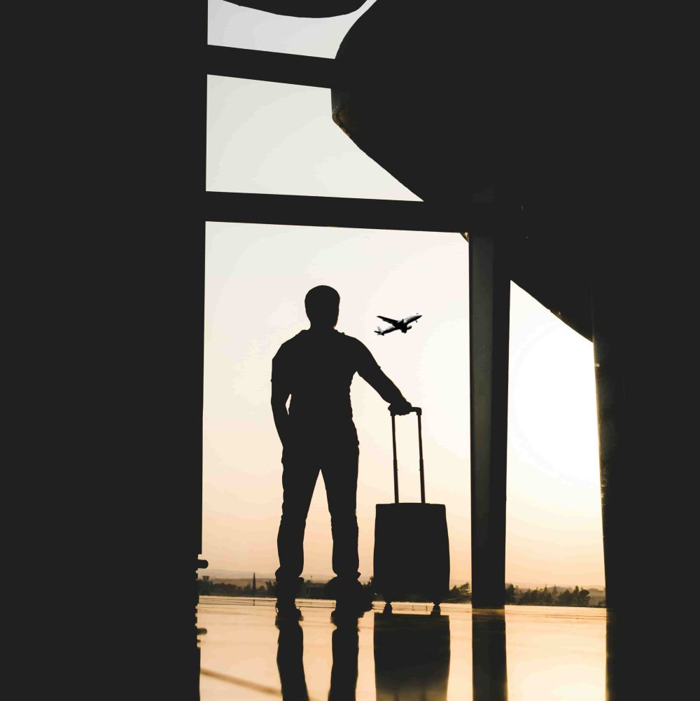 Die Sillhouette einer Person an einem Flughaufen. Draußen sieht man ein Flugzeug starten.