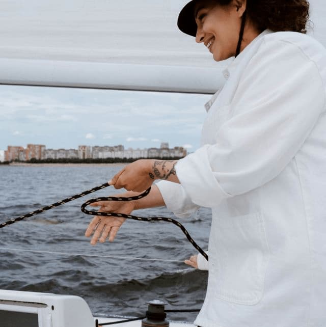 Eine Frau steht auf einem Boot und holt eine Leine ein.
